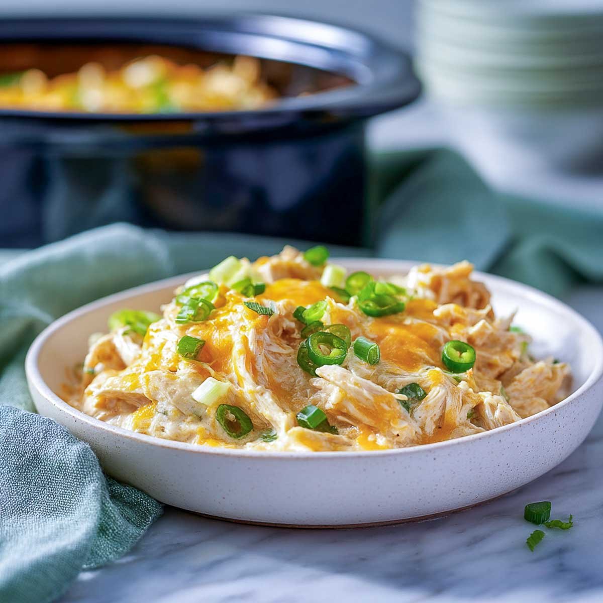 Shredded cheesy jalapeño chicken in a white bowl with melted cheese and green onions.