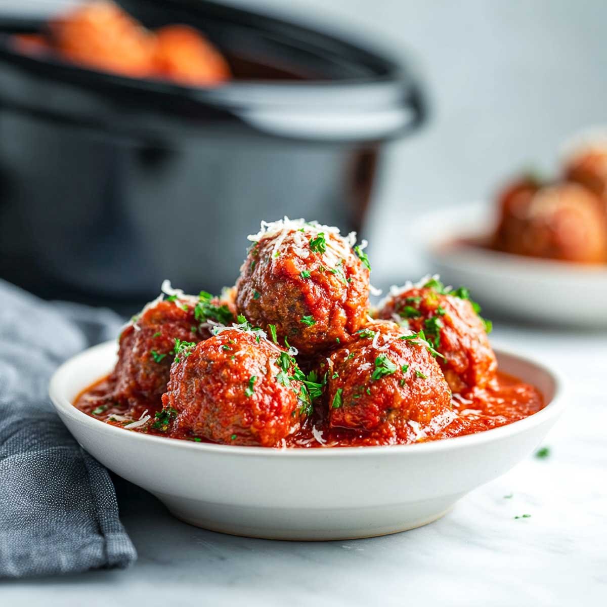 Meatballs in thick marinara with parmesan and parsley in a white bowl.