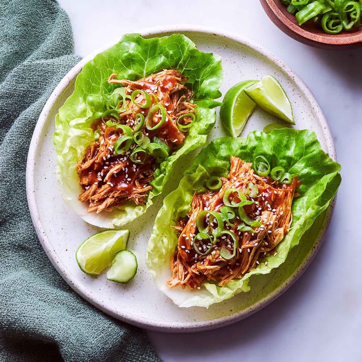 Top-down view of two crisp lettuce wraps filled with saucy pulled chicken and garnished with scallions and sesame seeds.