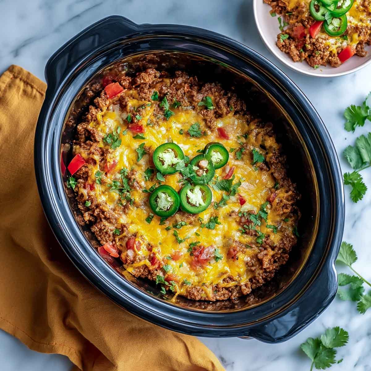 Top-down view of keto taco casserole inside a black crockpot with melted cheese and jalapeños.