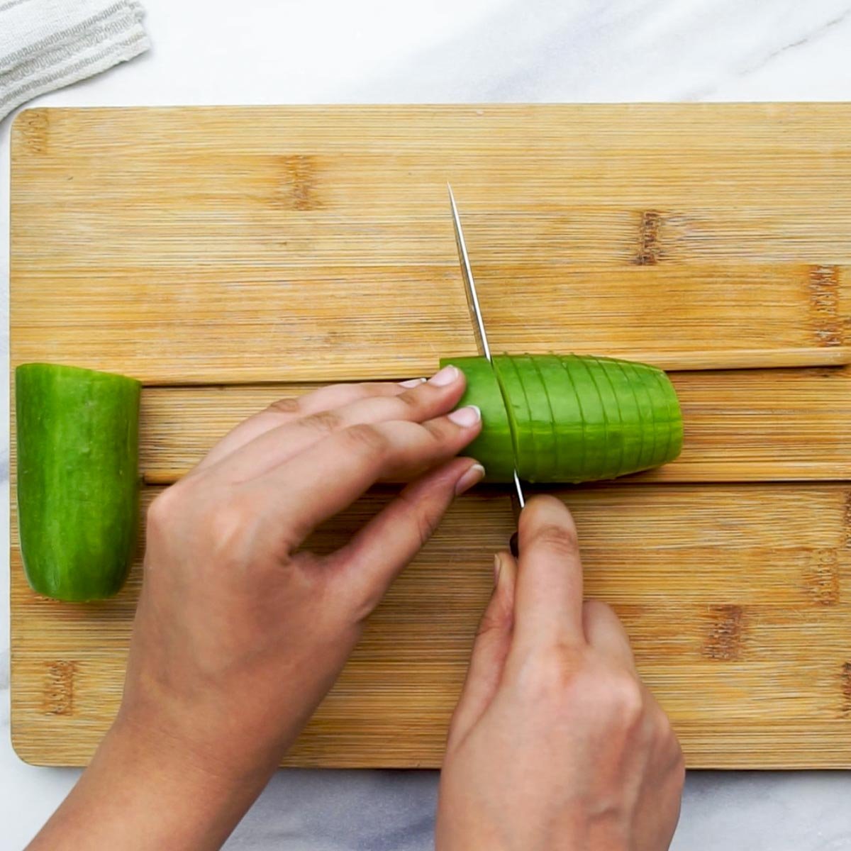 Using chopsticks as guides to make vertical cuts on a cucumber for accordion slicing.
