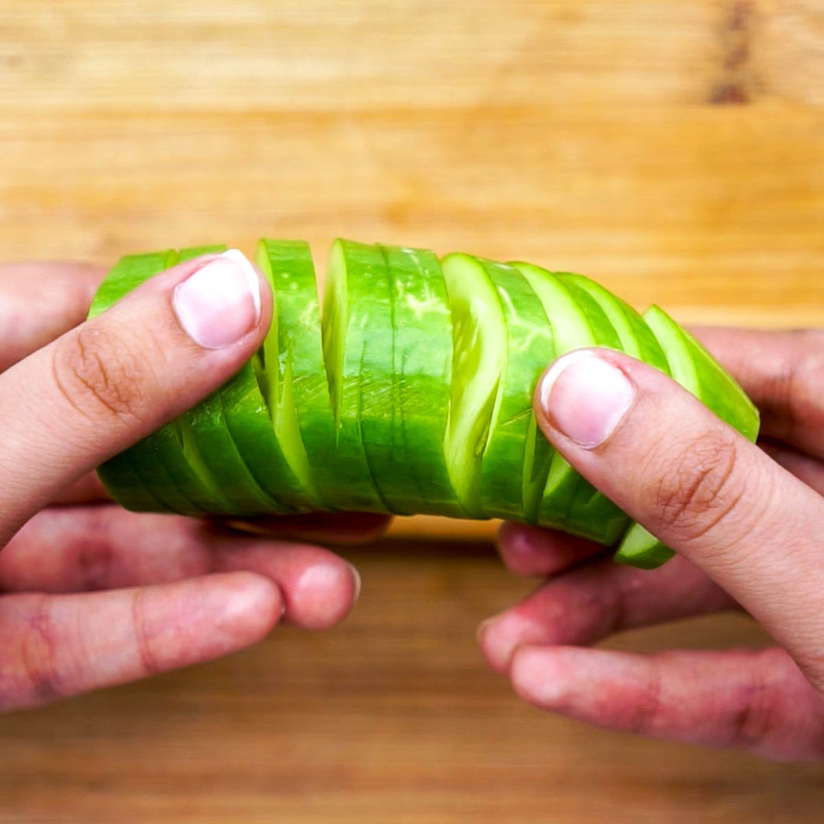 Hands gently spreading a cucumber to reveal the accordion pattern after slicing.