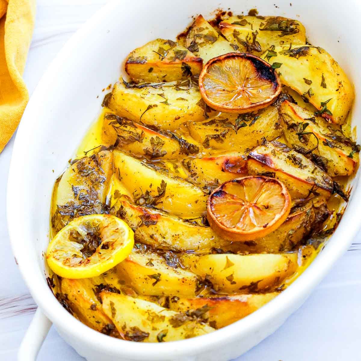 Close-up angle of roasted lemon Greek potatoes with caramelized lemon slices and herby oil.