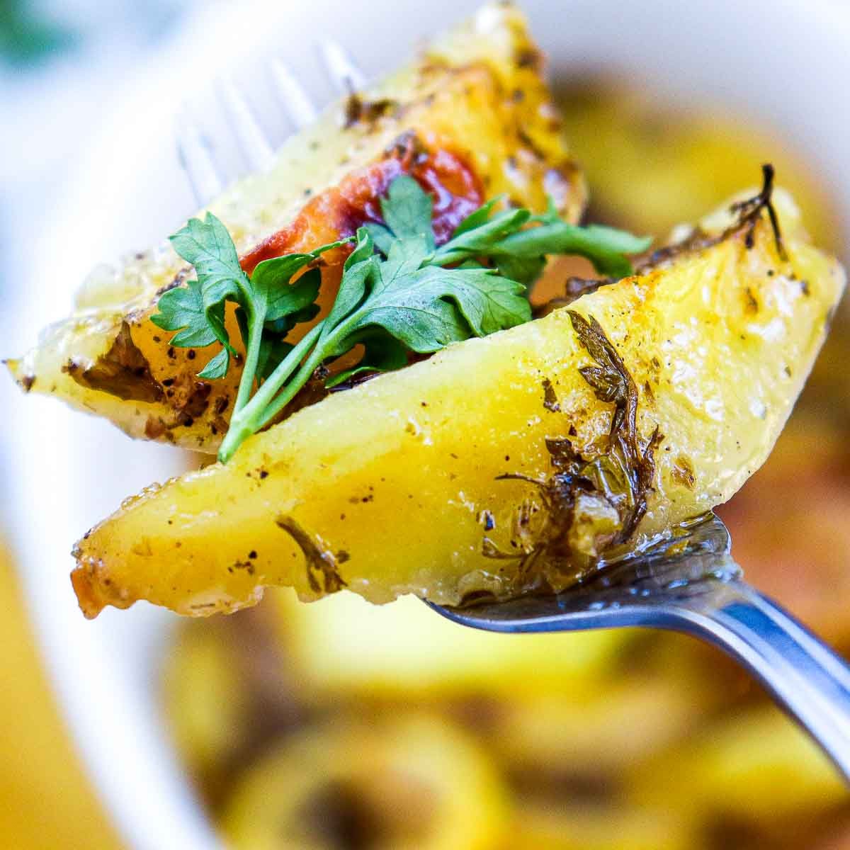 Fork holding a wedge of roasted lemon Greek potato topped with fresh parsley.