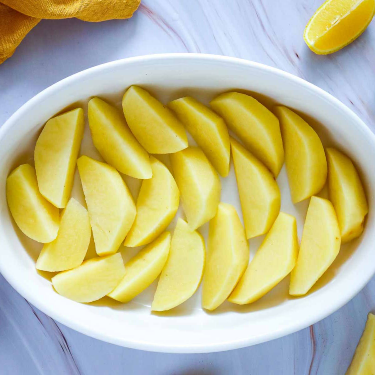 Raw potato wedges arranged in a single layer inside a white oval baking dish, ready for seasoning.