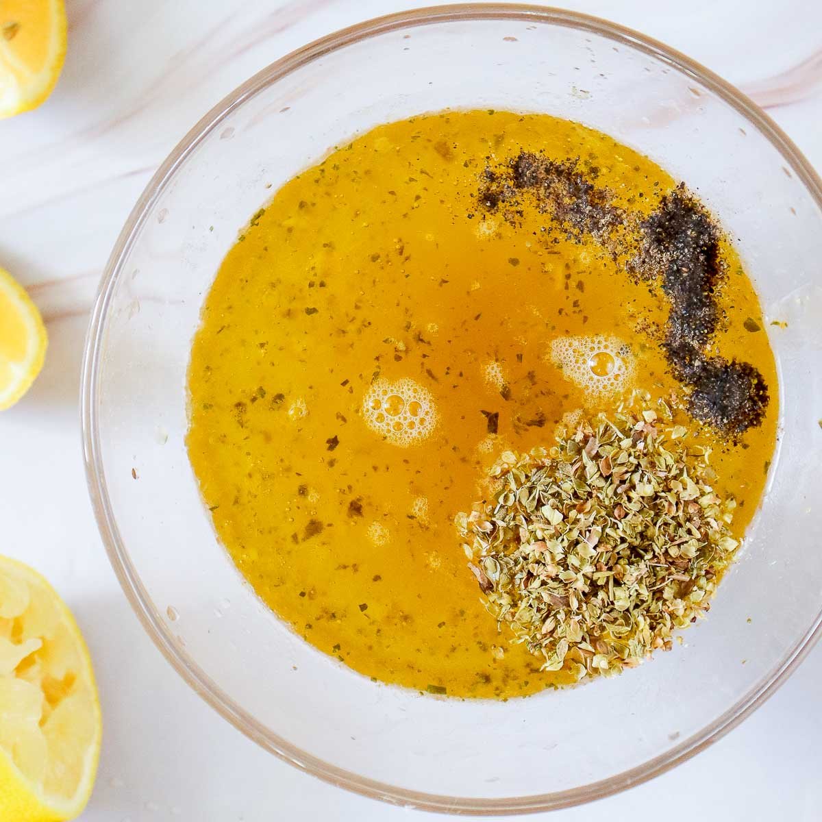 Bowl of marinade with olive oil, broth, lemon juice, oregano, salt, and pepper before being mixed.