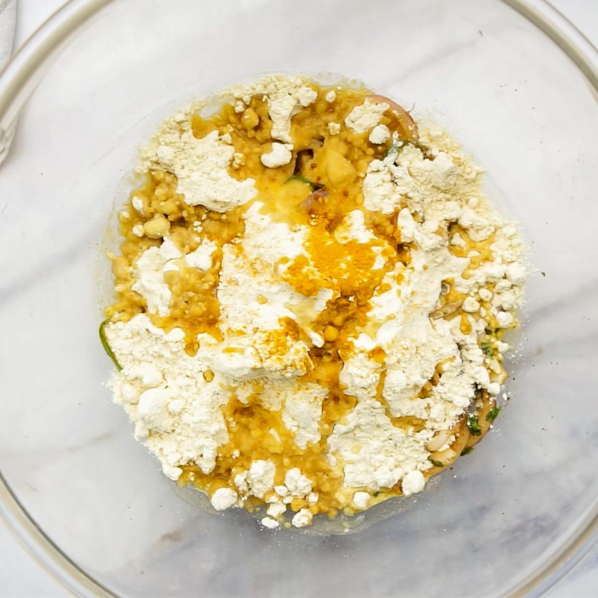 Besan (chickpea flour), turmeric, and other ingredients added to the spiced onion mixture in a glass bowl.