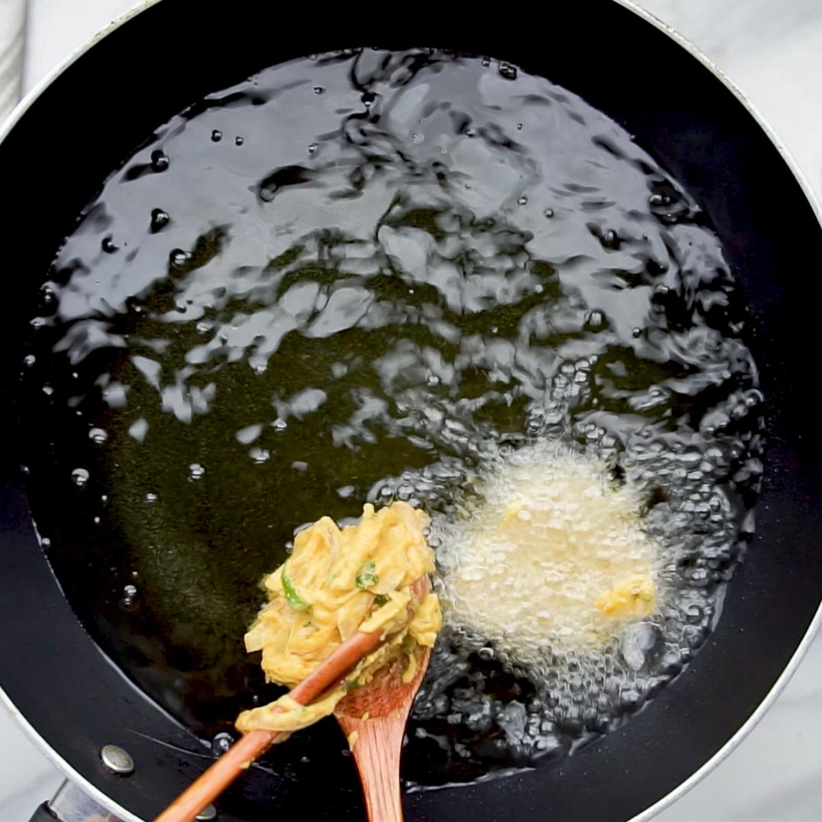 Spoonful of pakora batter being dropped into hot oil for deep frying.