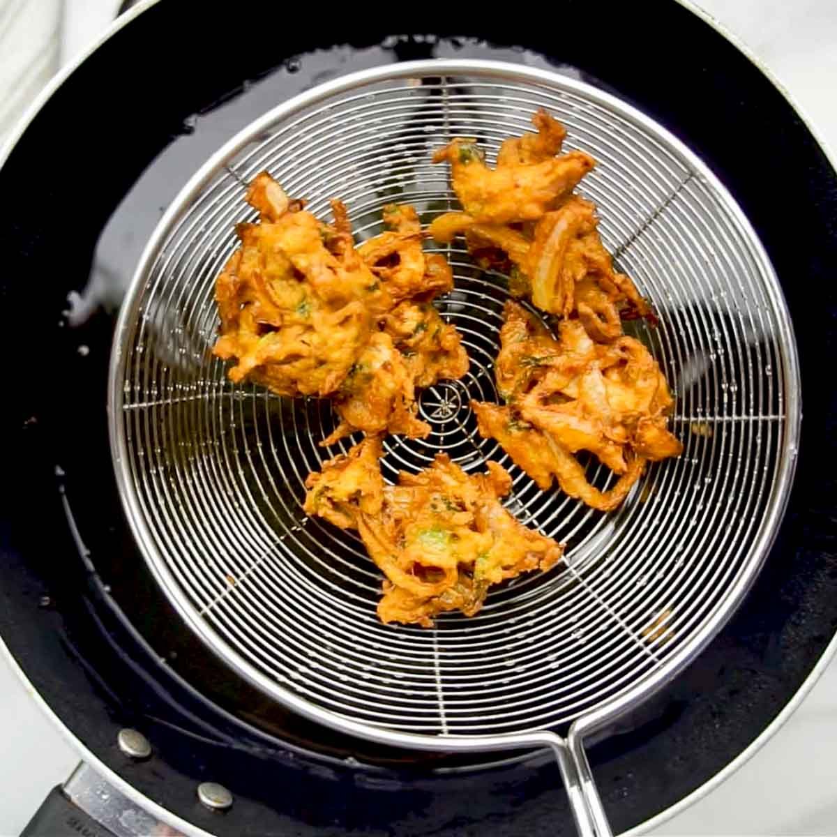Freshly fried onion pakoras resting on a slotted ladle over hot oil.
