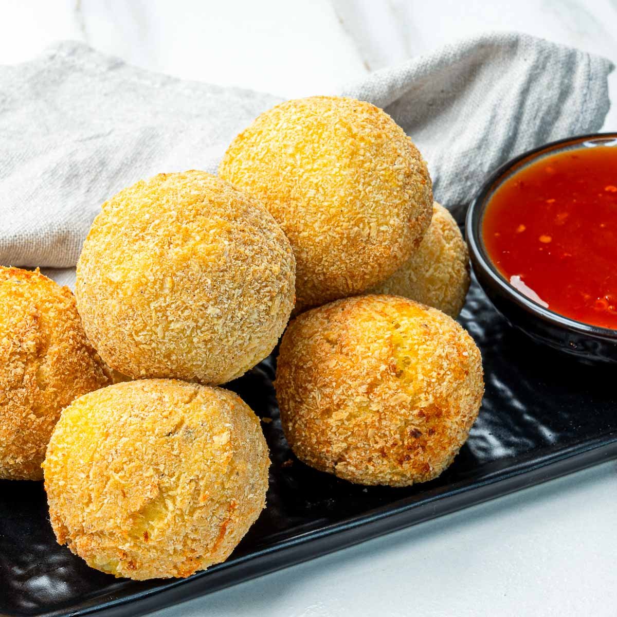 Crispy golden potato cheese croquettes stacked on a black plate with dipping sauce.
