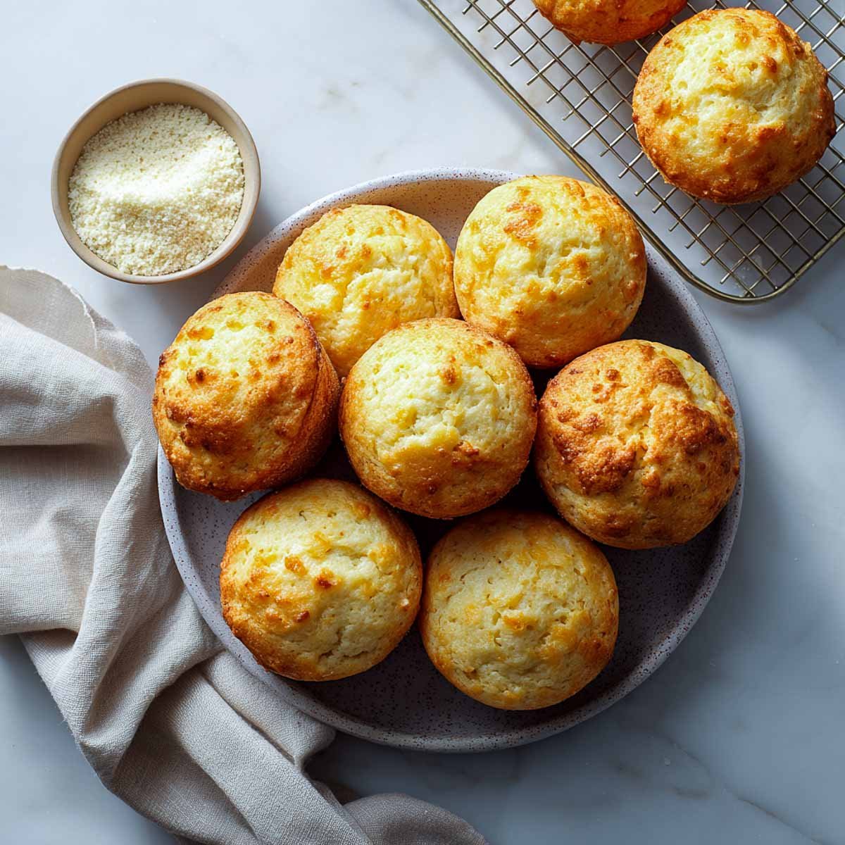 Top-down view of plain savory muffins with cottage cheese and flour bowl on a marble surface.