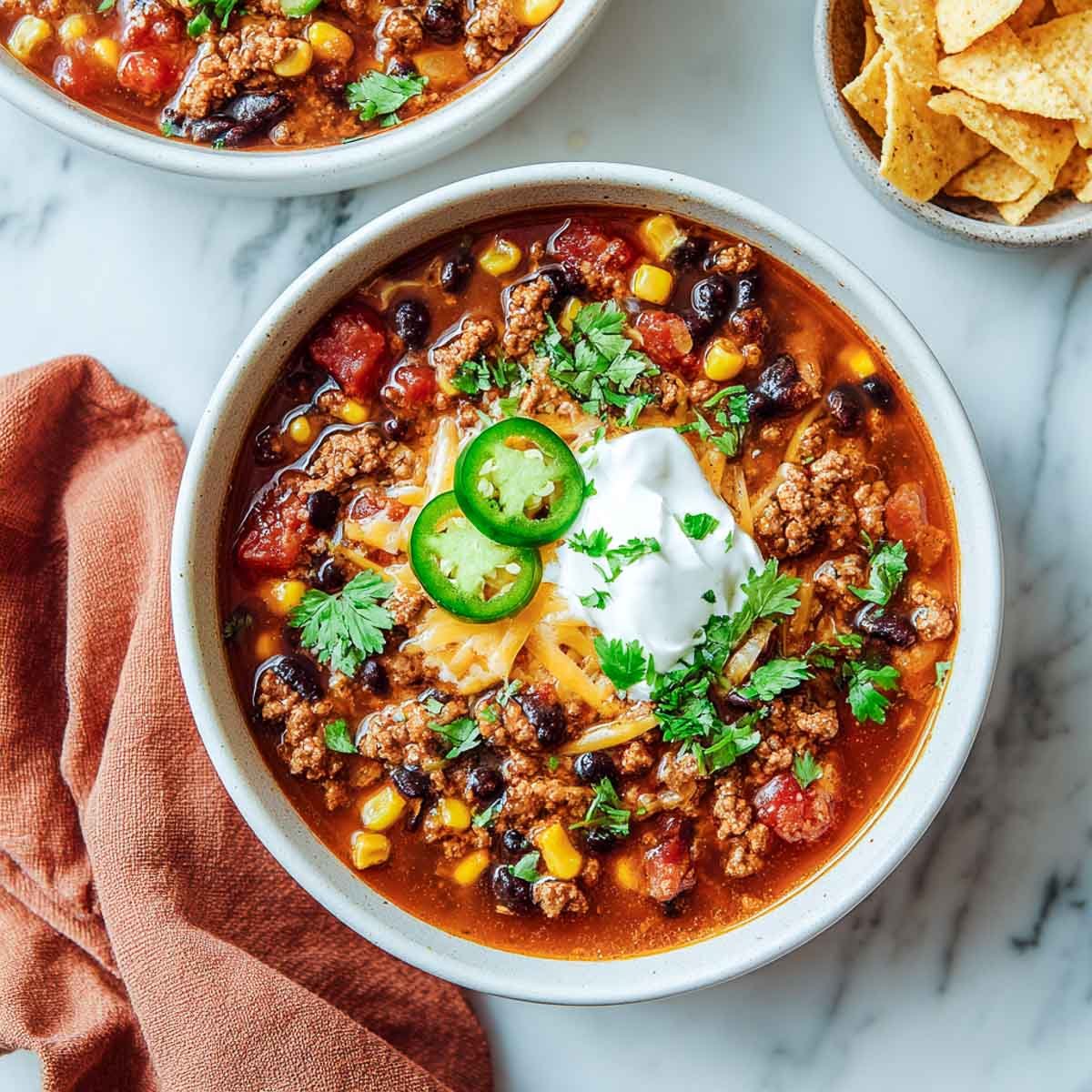 Taco soup with ground turkey, beans, corn, and toppings in a white bowl.