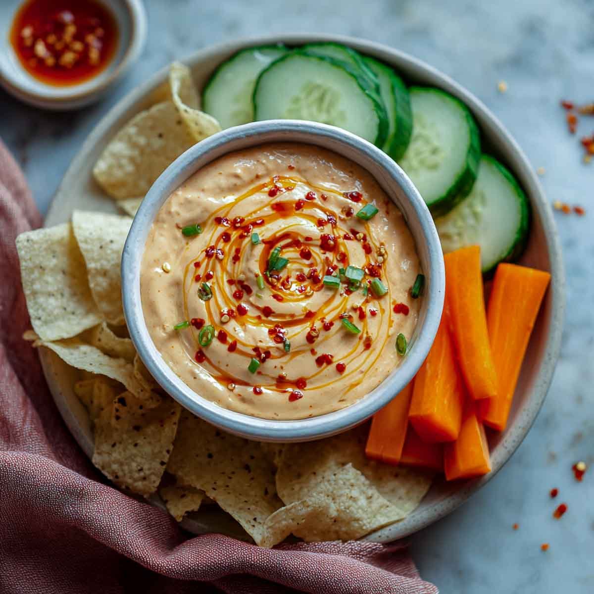 Creamy sriracha dip with chili swirl, served with chips, cucumbers, and carrots.