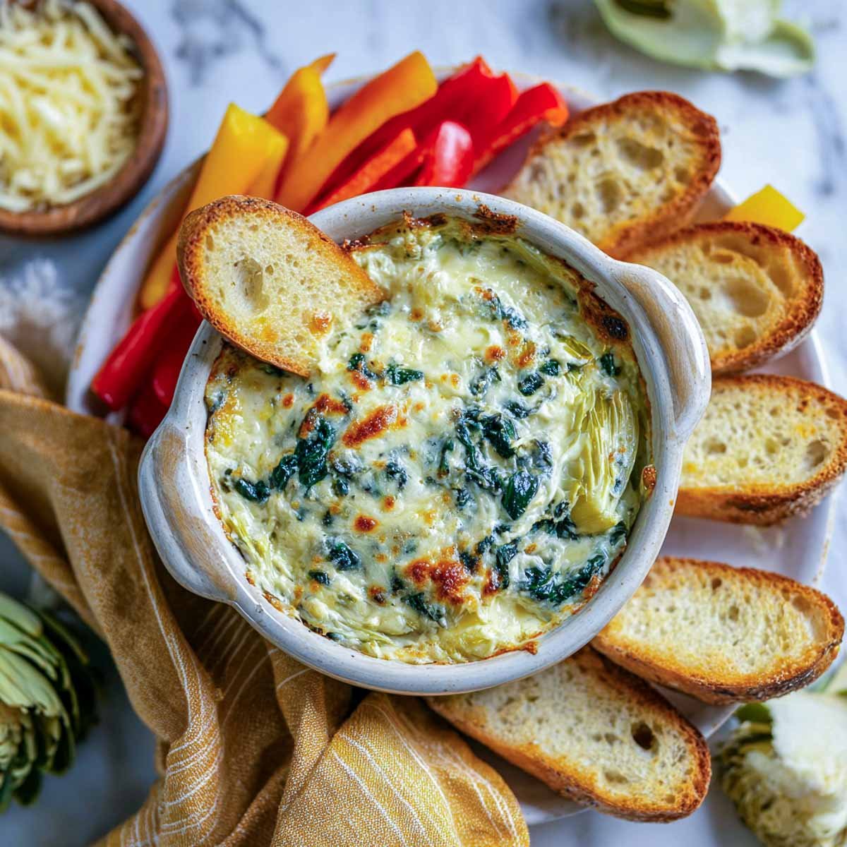 Baked spinach artichoke dip with toasted bread and bell pepper strips.