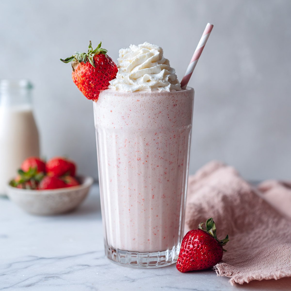 Side-angled view of a tall glass strawberry milkshake with fresh berries and straw.