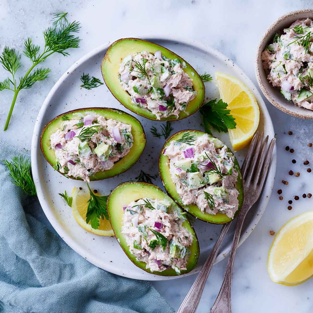 Top-down view of halved avocados filled with tuna salad and fresh herbs.