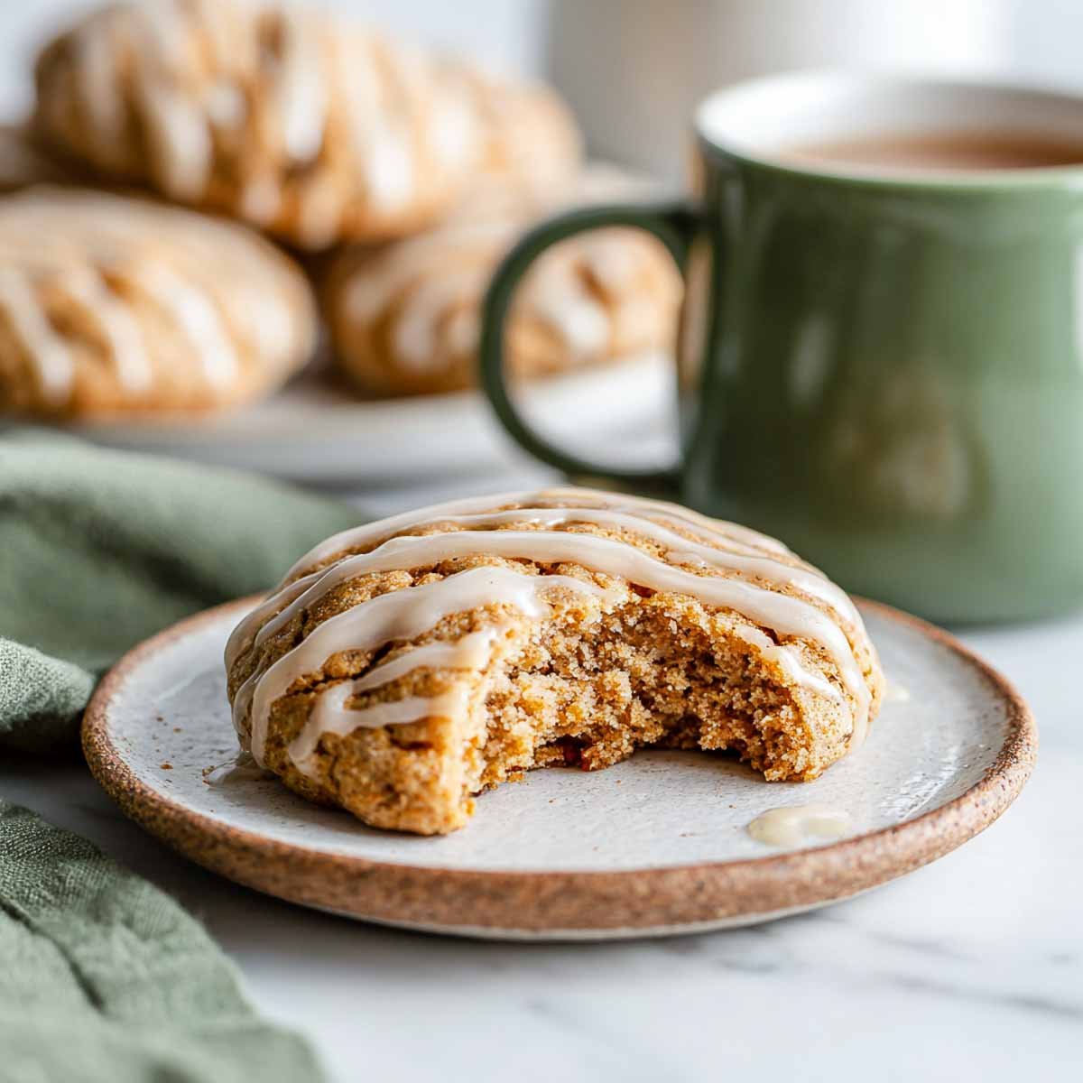 Close-up of bitten apple cider cookie with brown sugar glaze on ceramic plate.