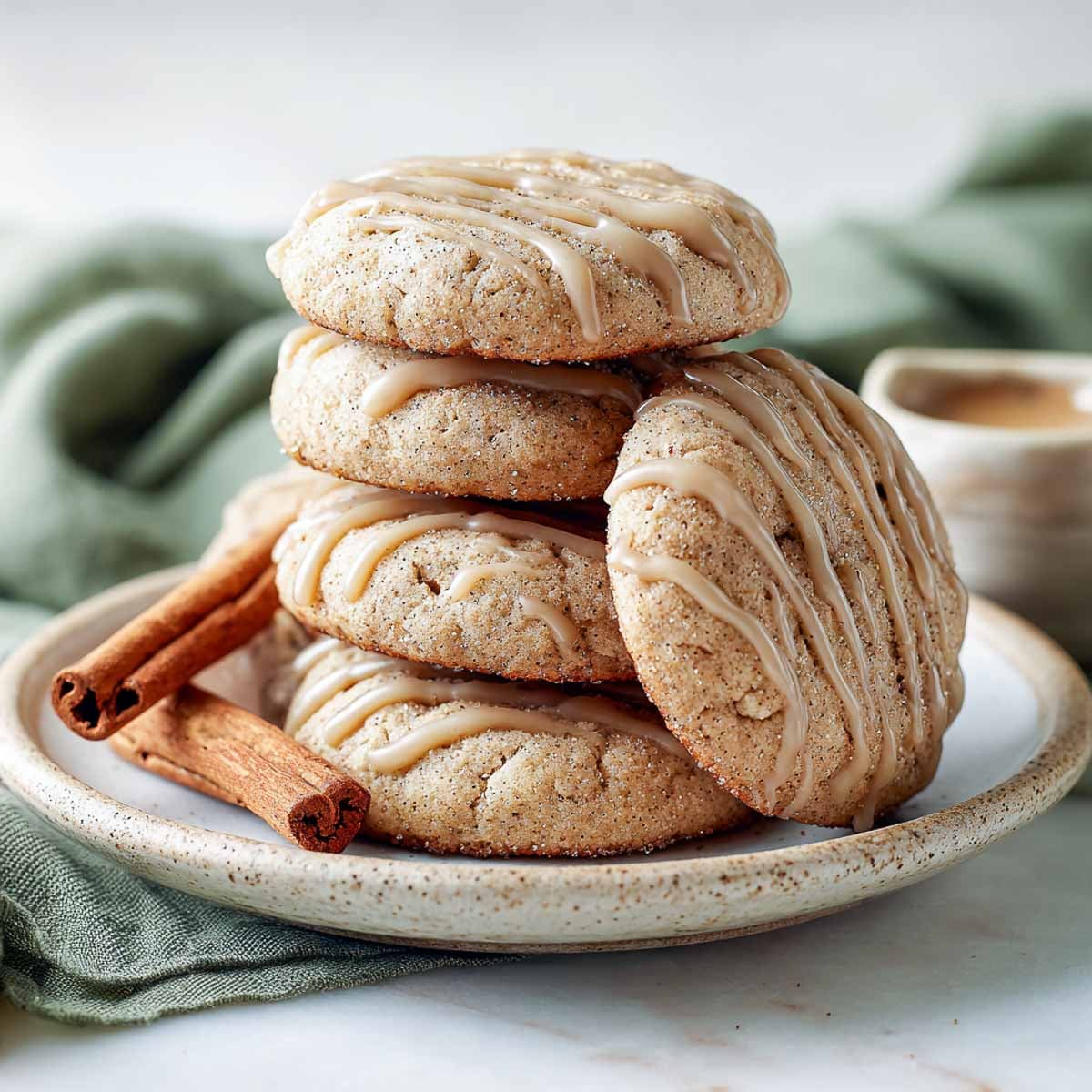 Stack of apple cider cookies with glaze, cinnamon sticks, and green napkin.