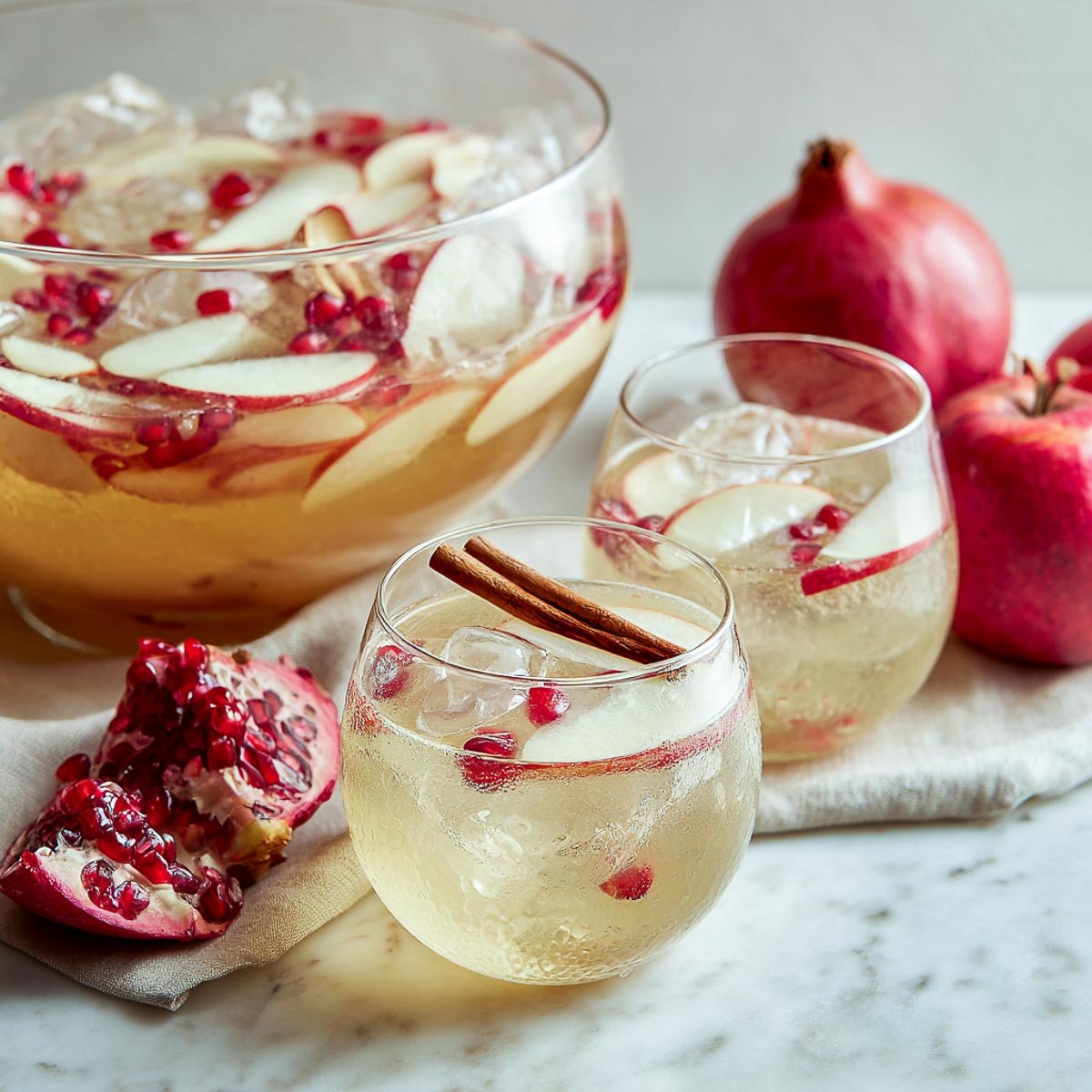 Glass of apple gin punch with pomegranate and cinnamon on marble.