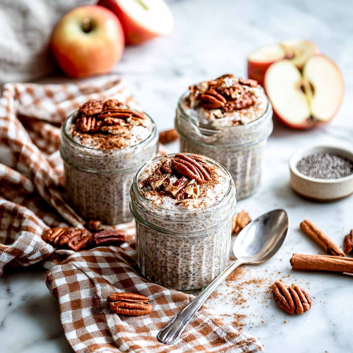 Three small jars of chia pudding topped with pecans on a marble surface.