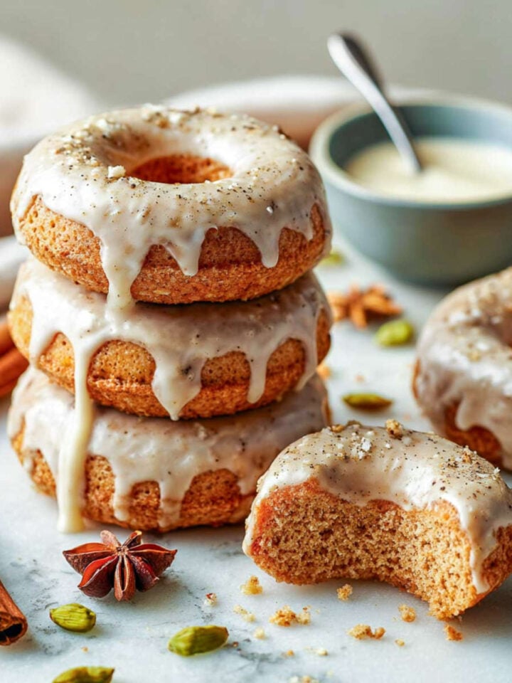 Close-up of stacked baked chai spiced donuts with vanilla glaze and cardamom pods.