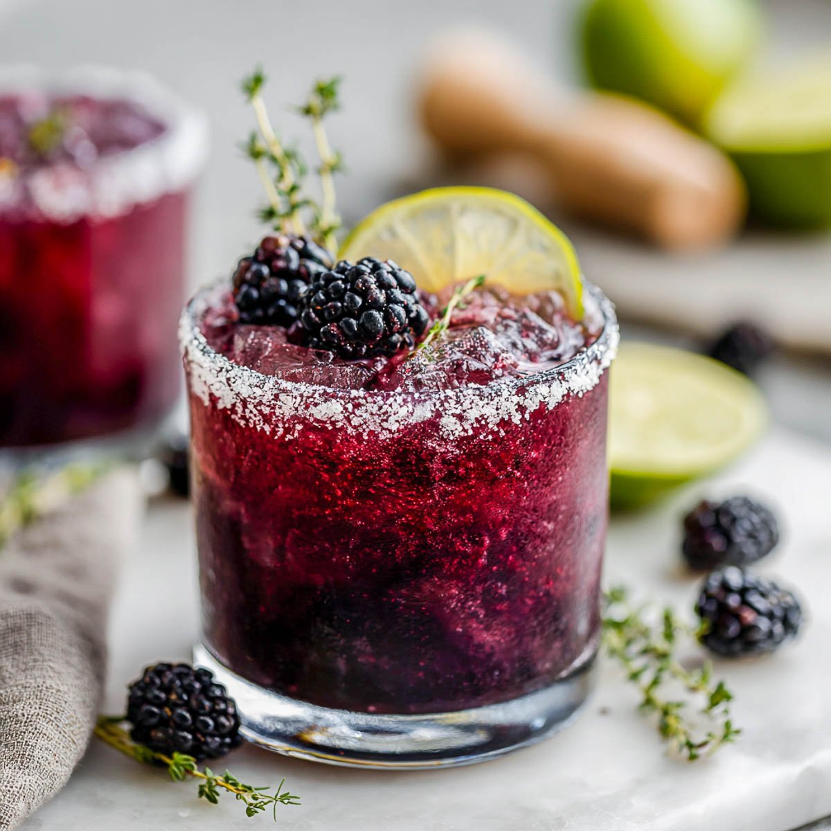 Blackberry margarita with lime slice, thyme, and crushed ice in glass.