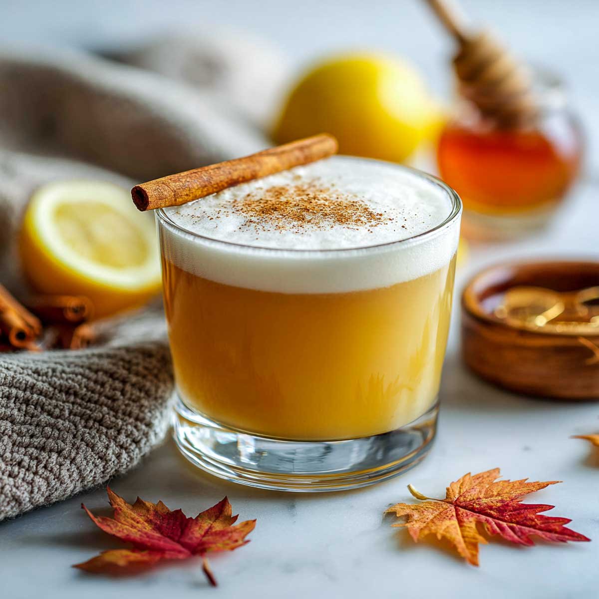 Tequila sour cocktail with foam top, cinnamon stick, and honey and lemon in the background.