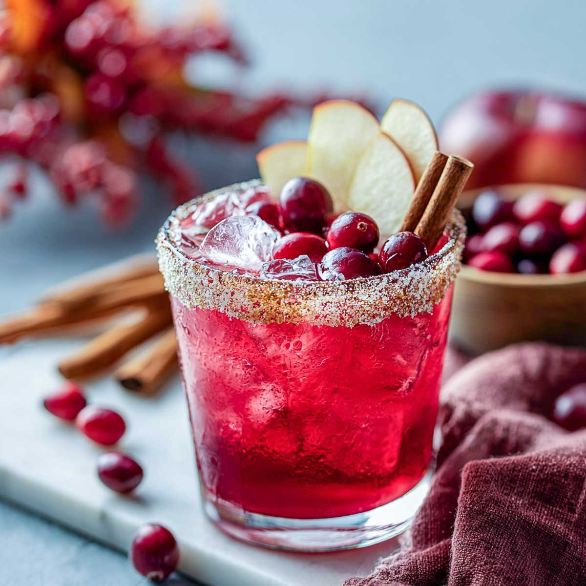 Vibrant cranberry apple margarita with apple slices and cranberries on top.