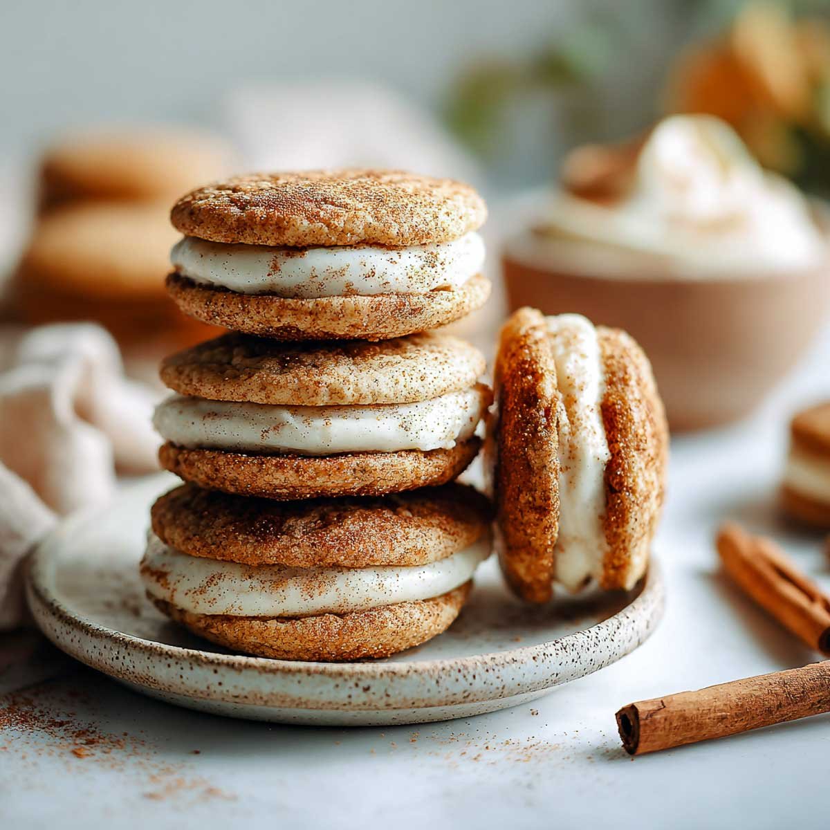 Soft snickerdoodle sandwich cookies filled with creamy maple frosting on ceramic plate.