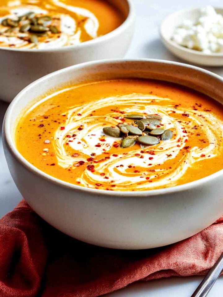 Side view of pumpkin soup in bowl with pepitas and red pepper flakes.