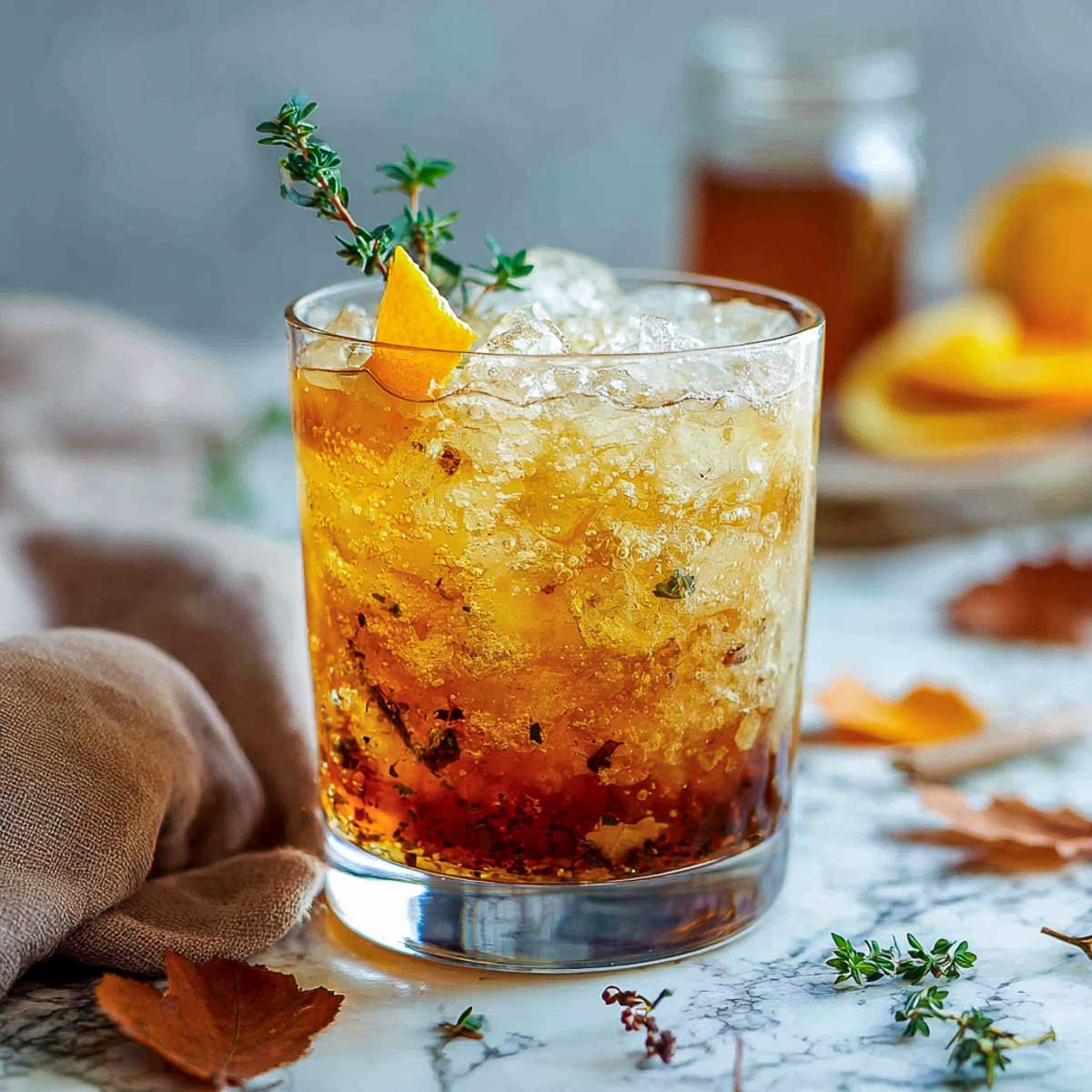 Bourbon smash cocktail with orange zest and thyme on crushed ice.