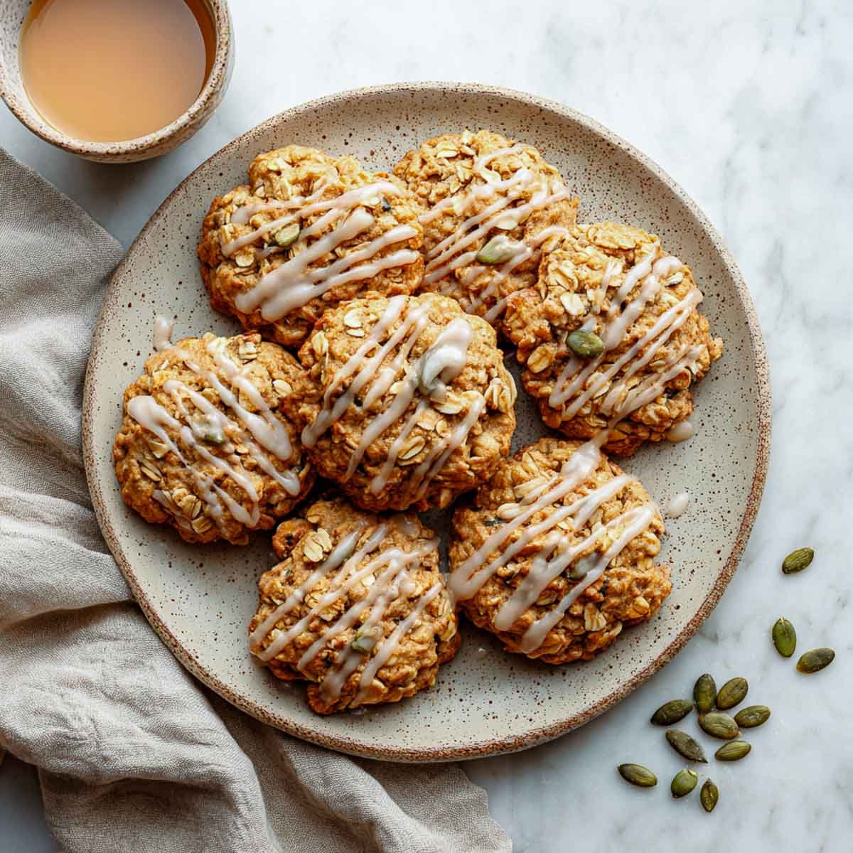 Soft-baked maple pumpkin oatmeal cookies drizzled with glaze on beige plate.