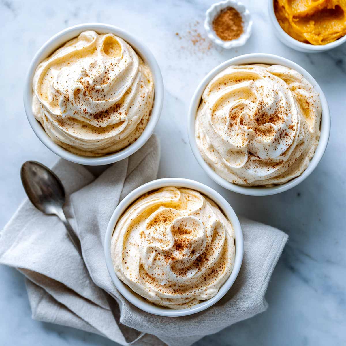 Top-down view of pumpkin cottage cheese whip served in three white bowls.