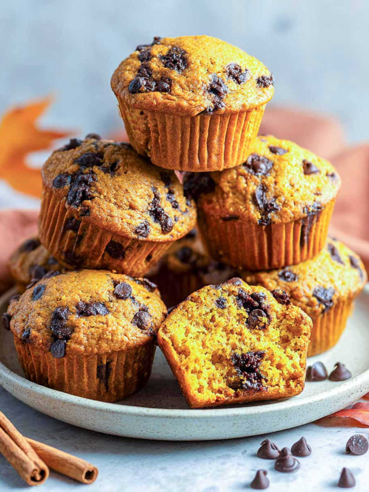 Close-up of stacked pumpkin chocolate chip muffins on a plate with visible chocolate chips.