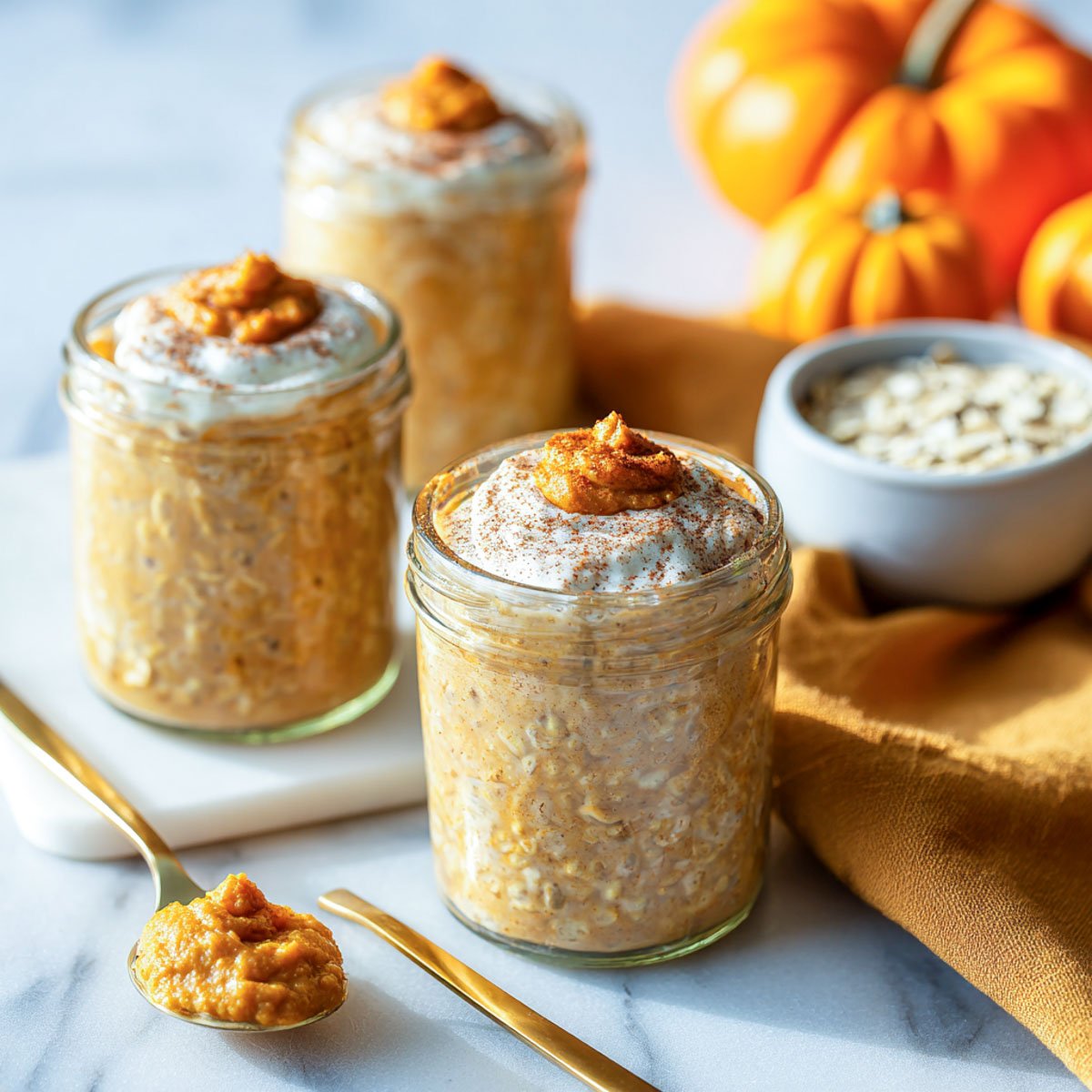 Three small glass jars of pumpkin cottage cheese overnight oats on marble surface.