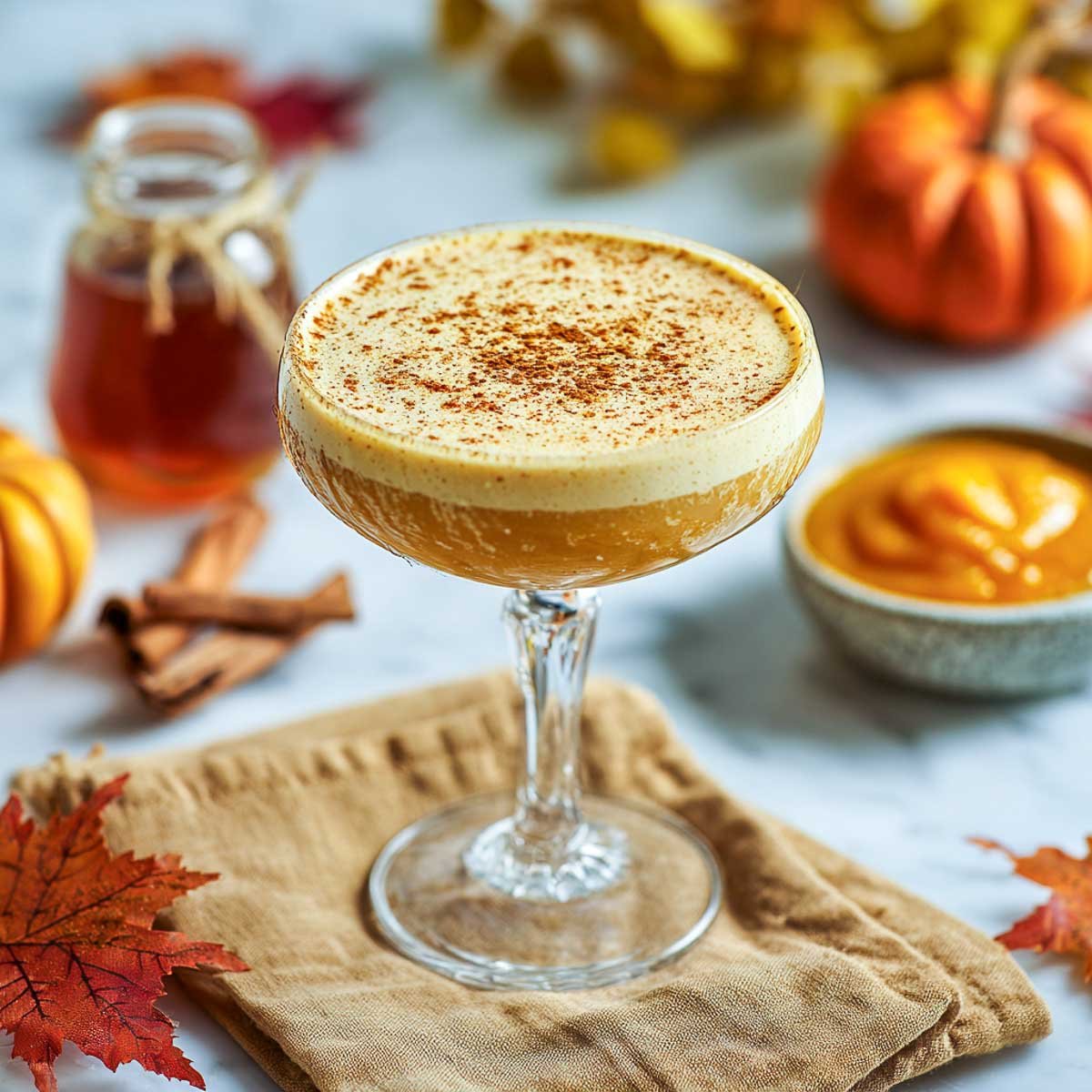 Pumpkin bourbon flip in a coupe glass with cinnamon dusting on foam top.