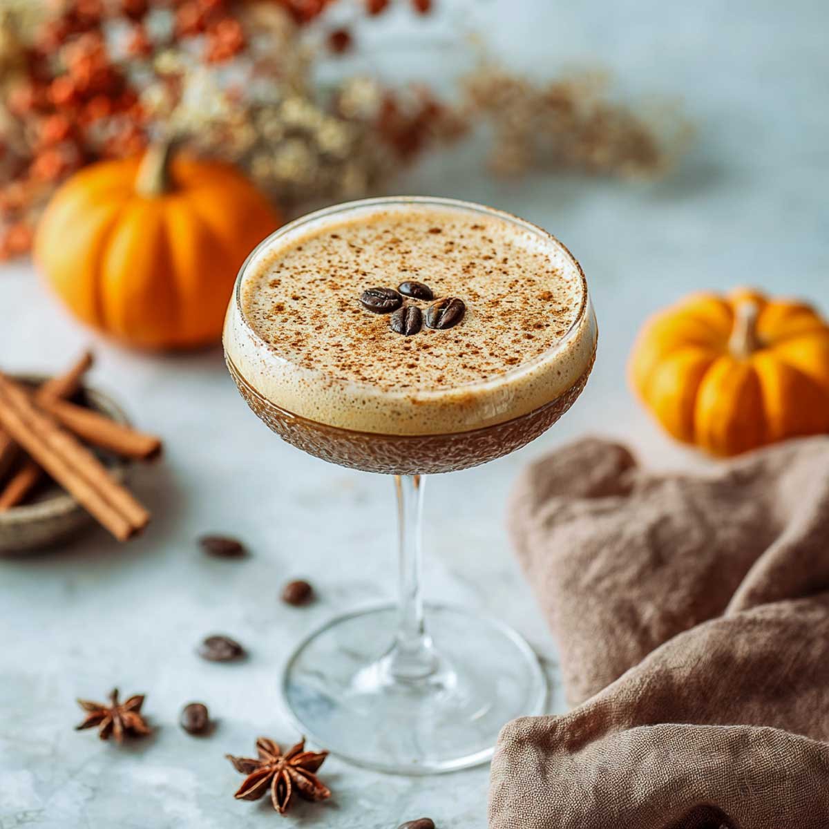 Pumpkin spice espresso martini with foam and coffee beans on marble surface.