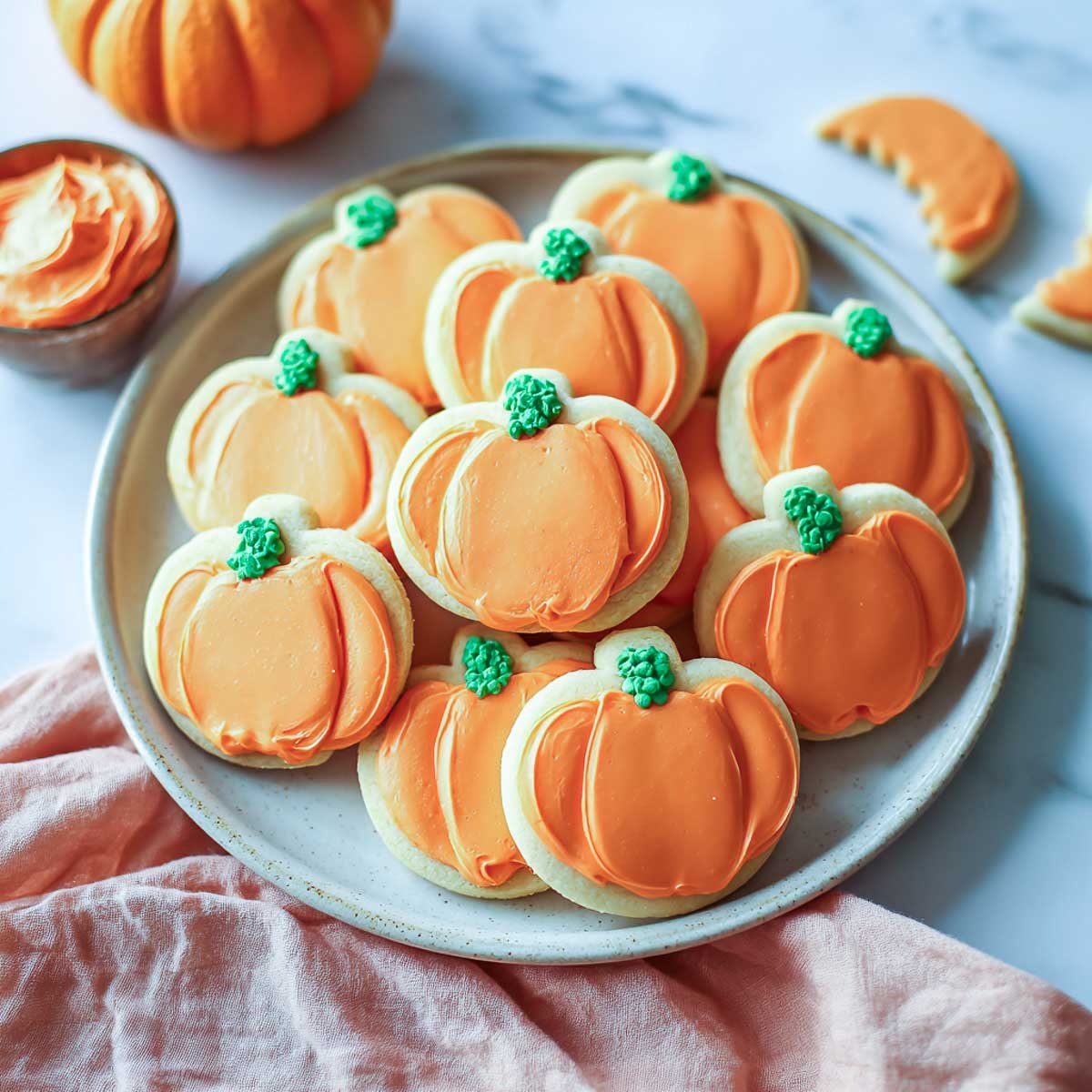 Pumpkin-shaped sugar cookies with orange frosting and green icing on top.