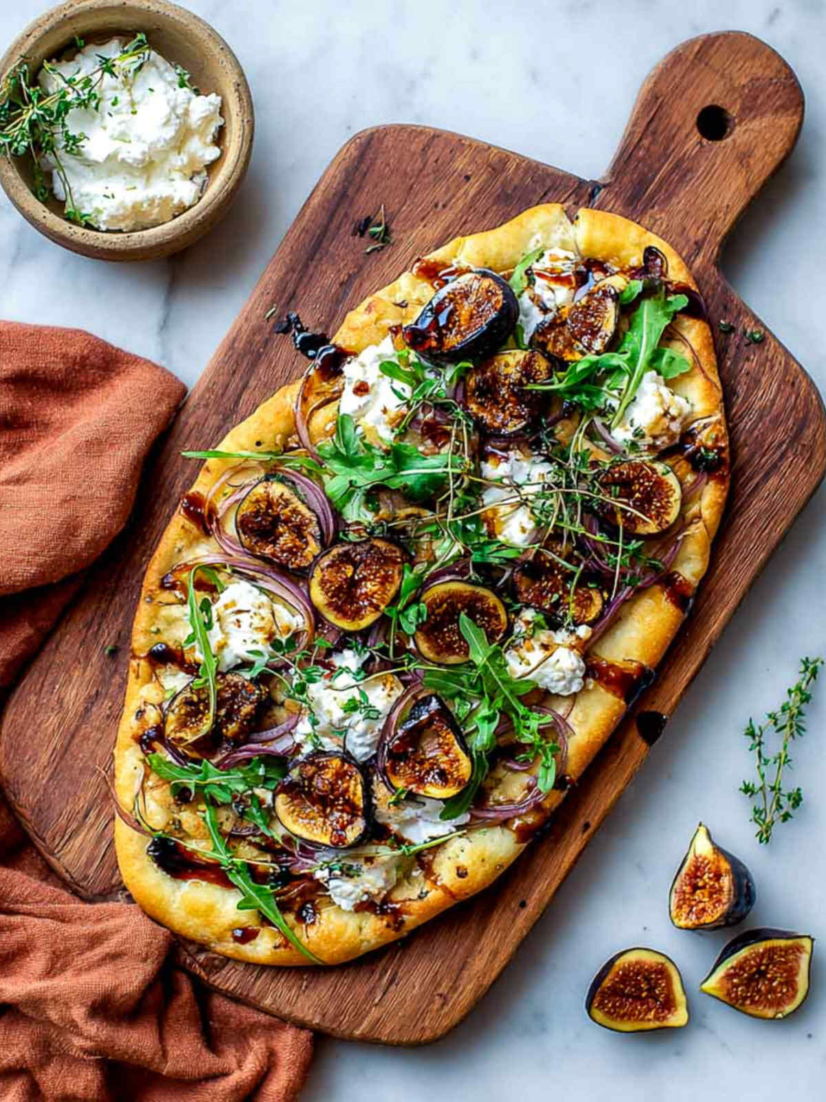 Flatbread with roasted figs and cottage cheese on board with fresh figs nearby.