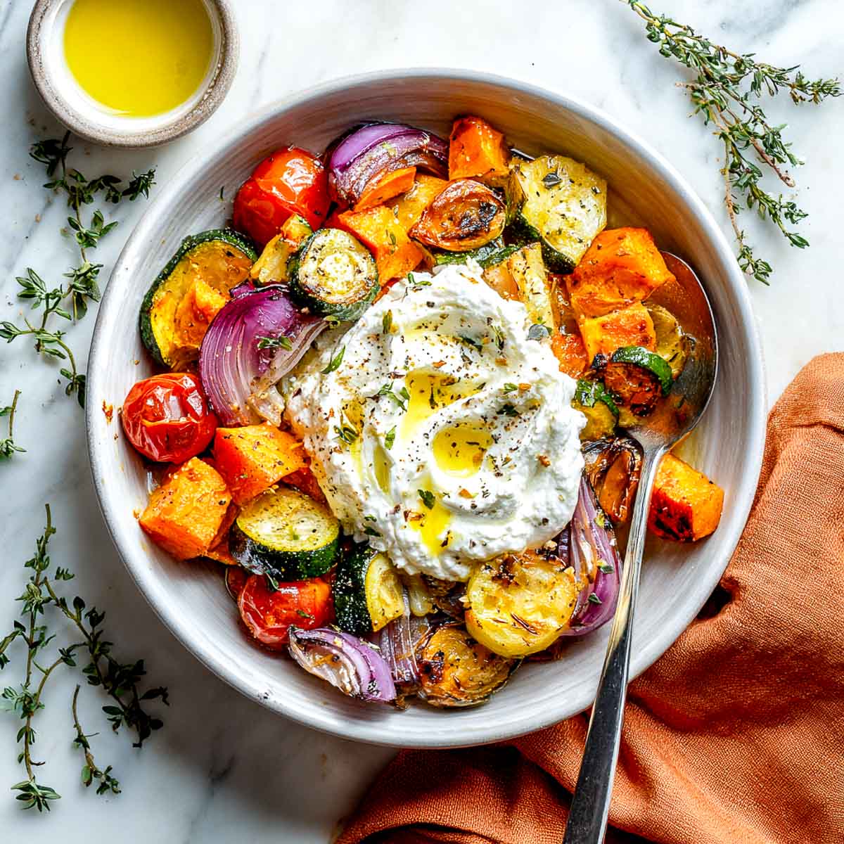 Roasted veggie bowl topped with seasoned cottage cheese and herbs.