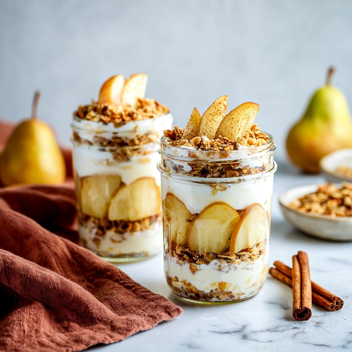 Side view of two glass jars layered with pears, granola, and cottage cheese.