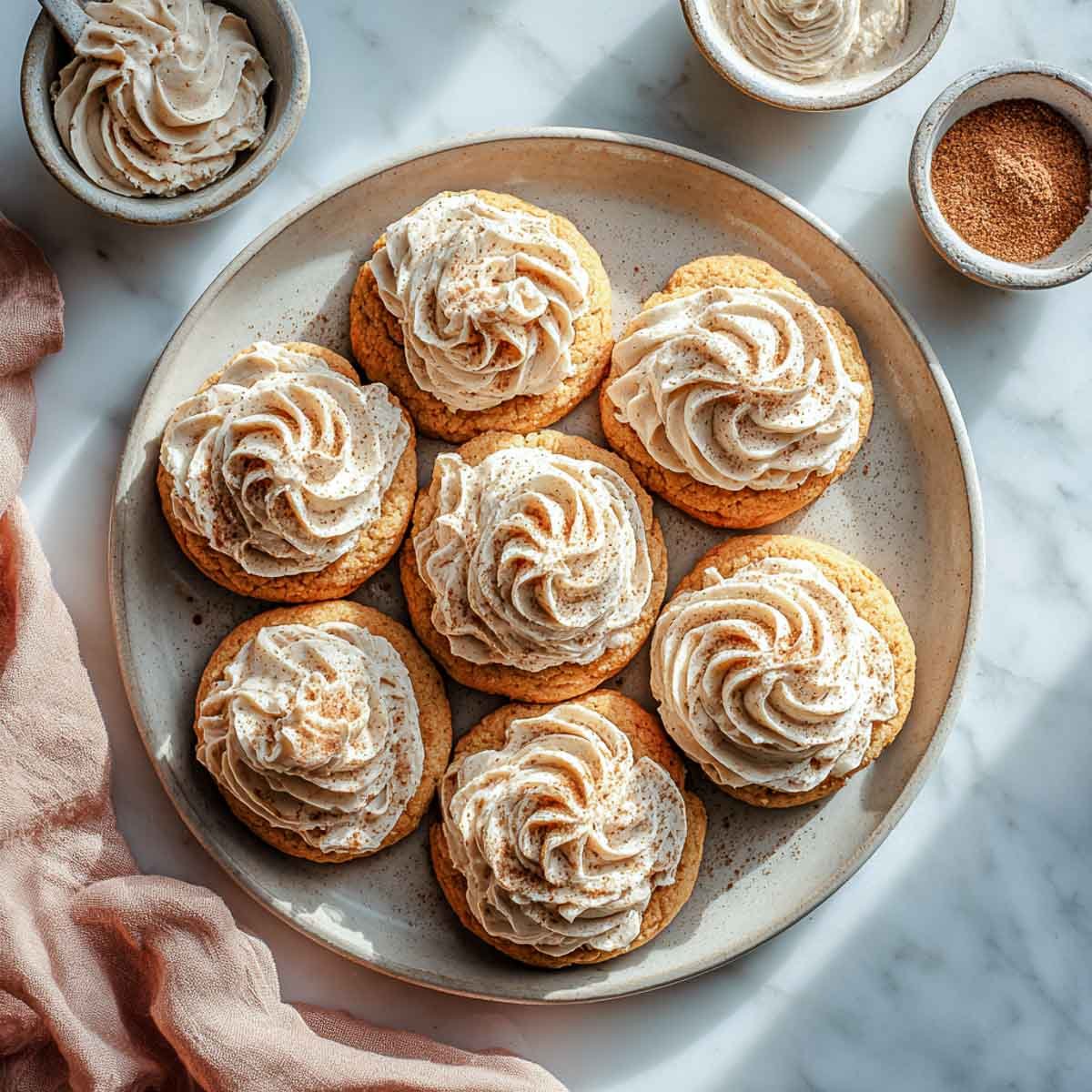 Soft pumpkin sugar cookies topped with maple frosting swirls on a ceramic plate.