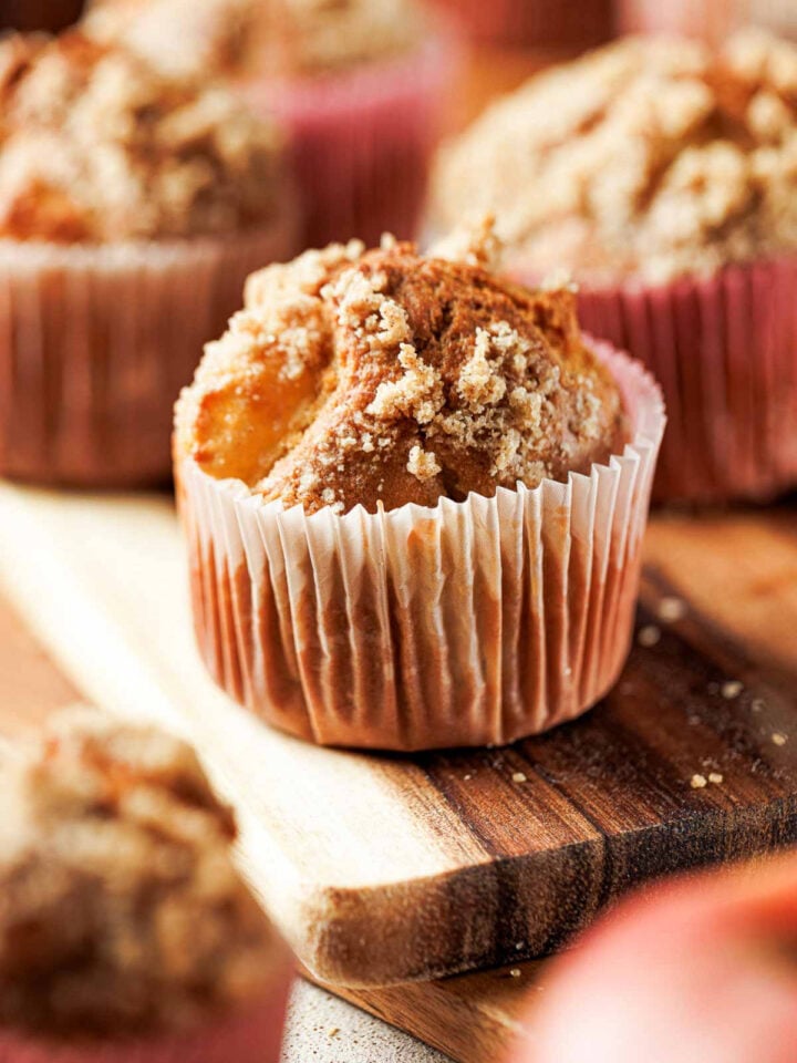 Close up of an apple cinnamon crumb muffin in a paper liner on a wooden board.