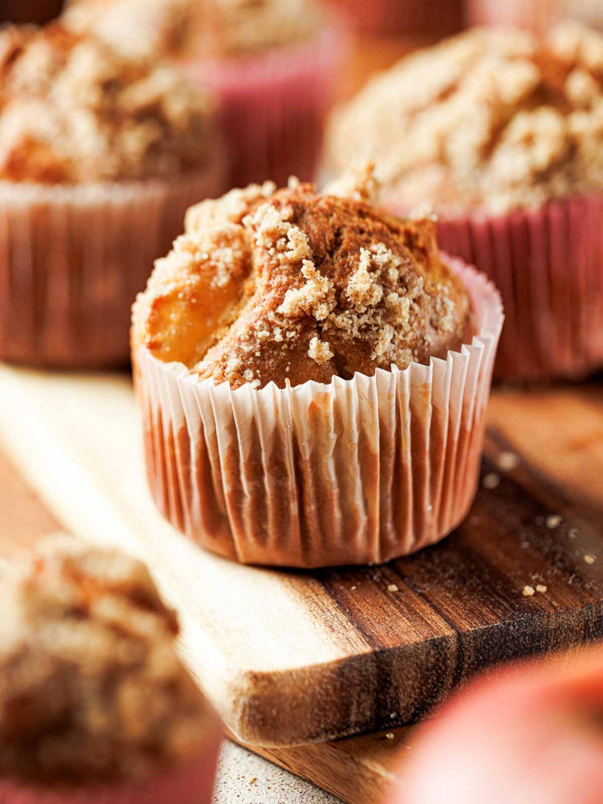 Close up of an apple cinnamon crumb muffin in a paper liner on a wooden board.