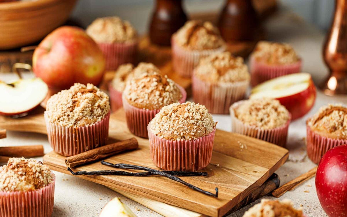 Freshly baked apple cinnamon crumb muffins on a wooden board with apples and cinnamon sticks.