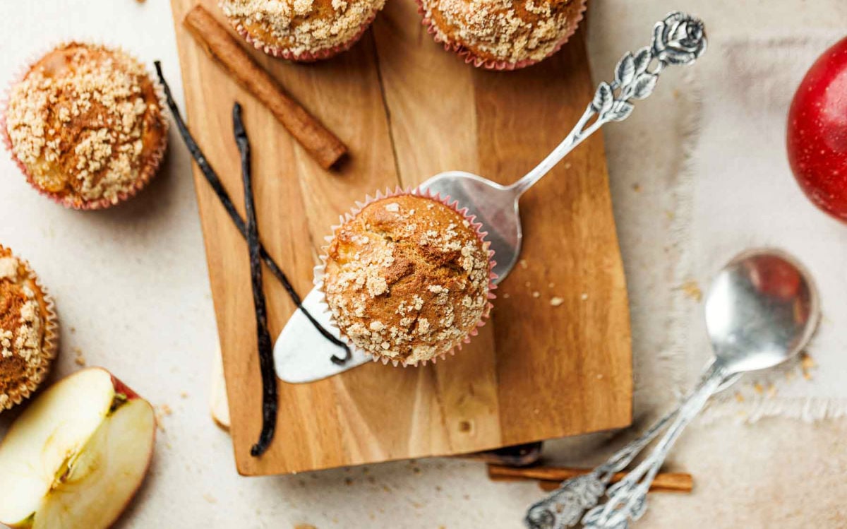 Overhead view of apple cinnamon muffin with crumb topping lifted from a wooden board.
