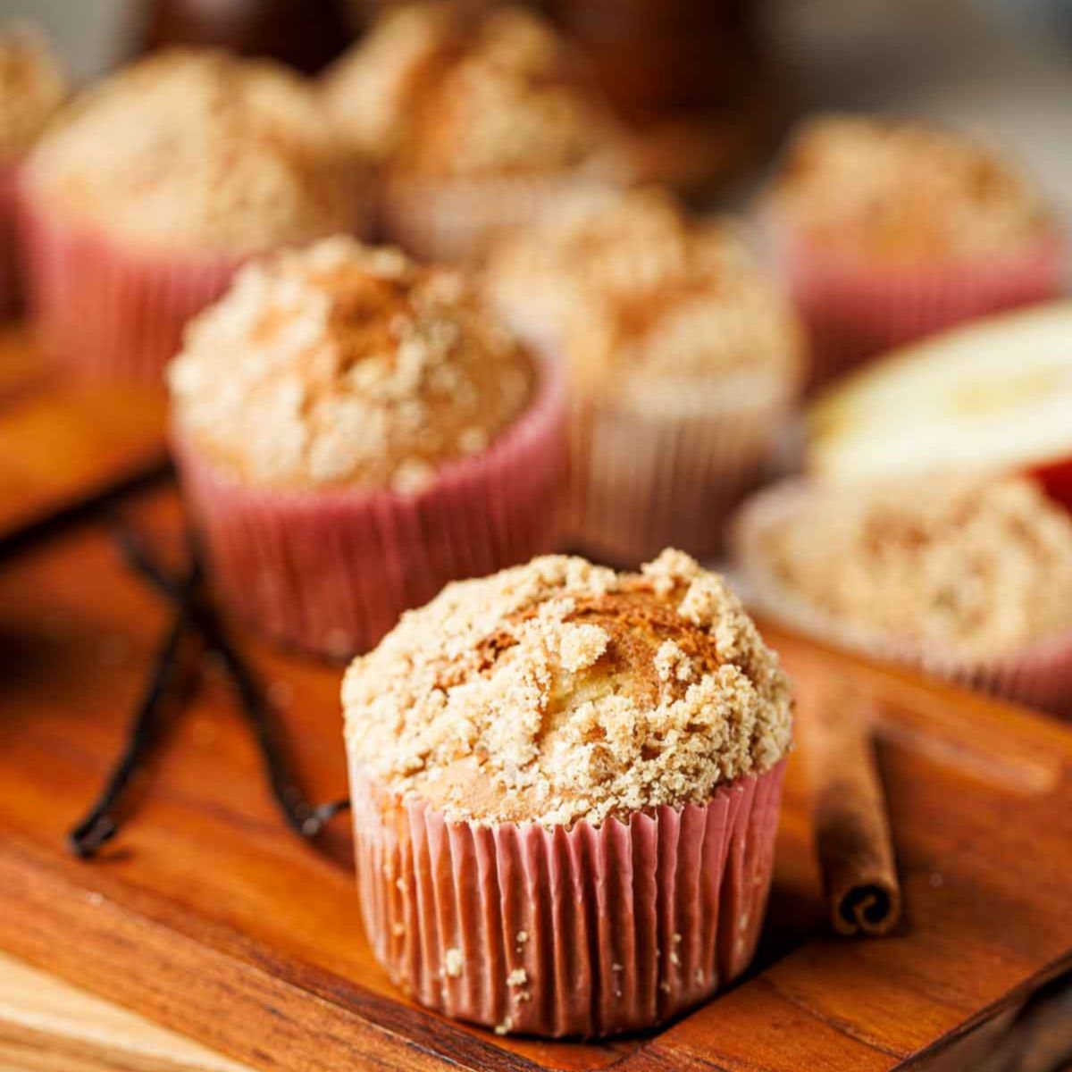 Bakery style apple cinnamon crumb muffin in a pink liner with a golden topping.