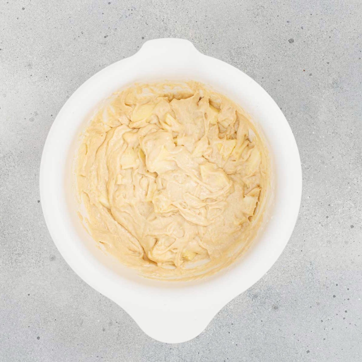 Apple cinnamon muffin batter with diced apples mixed in a white bowl.