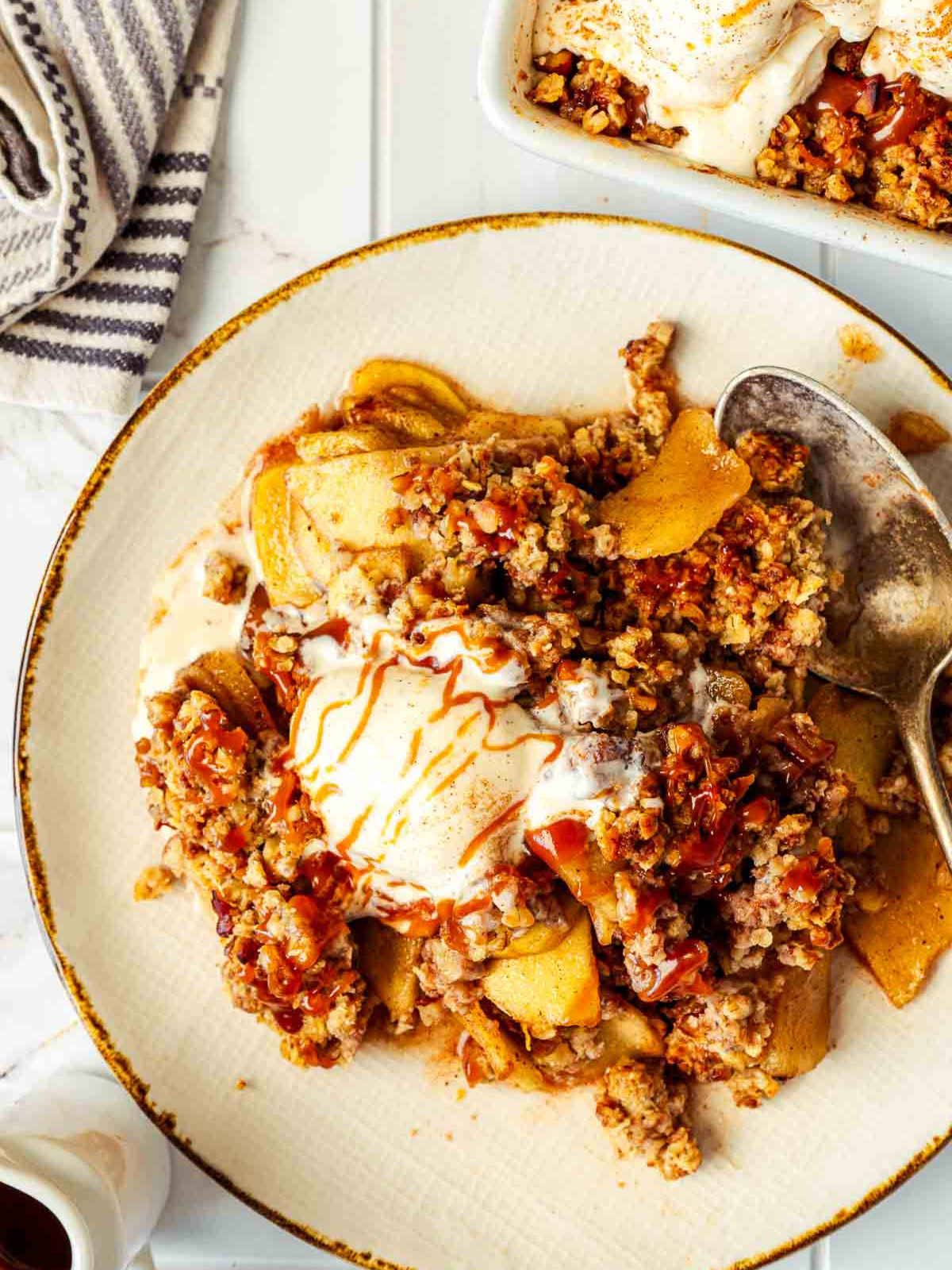 Plate of apple crisp with vanilla ice cream and caramel sauce, served with a spoon.