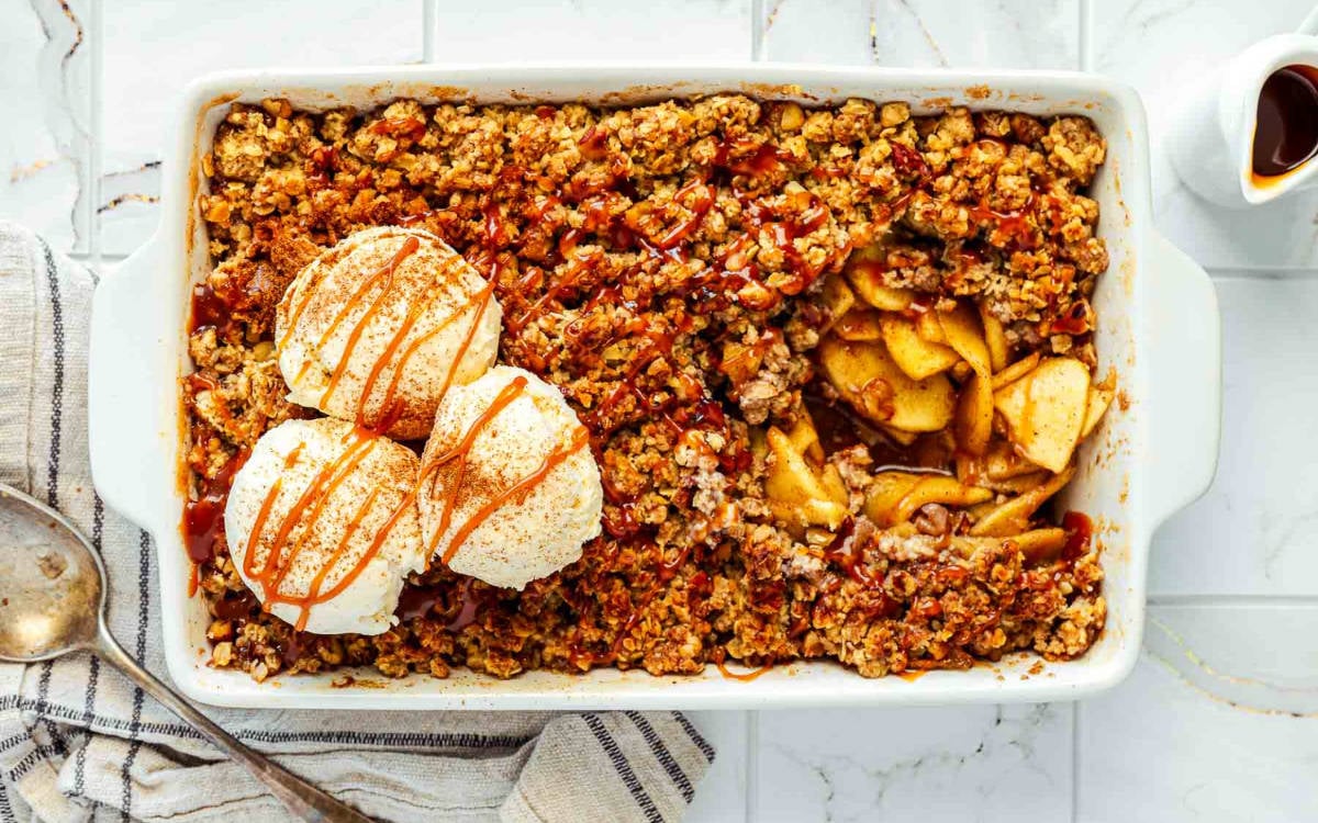 Overhead view of baked apple crisp in a dish with ice cream scoops and caramel drizzle.